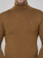 A person in a 98degreenorth Men’s Dark Khaki Merino Wool Turtle Neck Sweater with an embroidered chest logo.