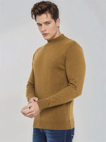 A man wears a 98degreenorth dark khaki merino wool turtleneck sweater with blue jeans, standing against a light background.