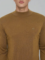 Man wearing 98degreenorth men’s dark khaki merino wool turtle neck sweater with chest logo, against a plain background.