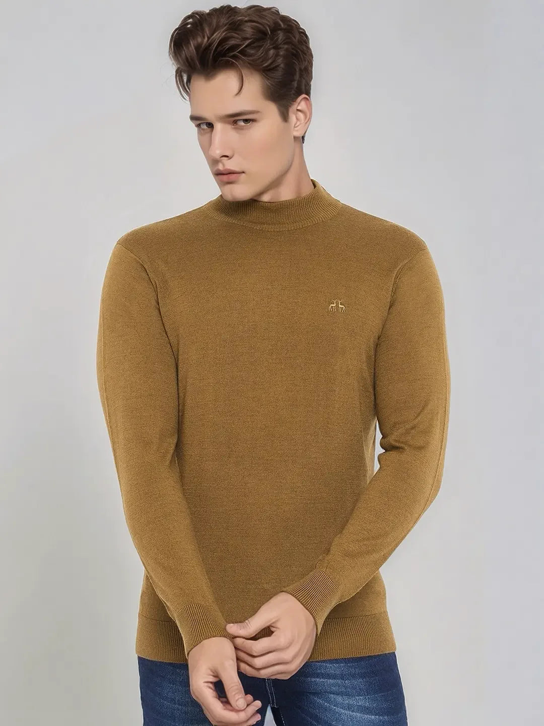 A man wears a 98degreenorth Men’s Dark Khaki Merino Wool Turtle Neck Sweater and blue jeans, against a light gray background.