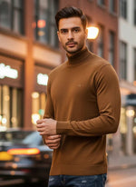A man wears the 98degreenorth Men’s Dark Khaki Merino Wool Turtle Neck Sweater on a city street with blurred buildings.