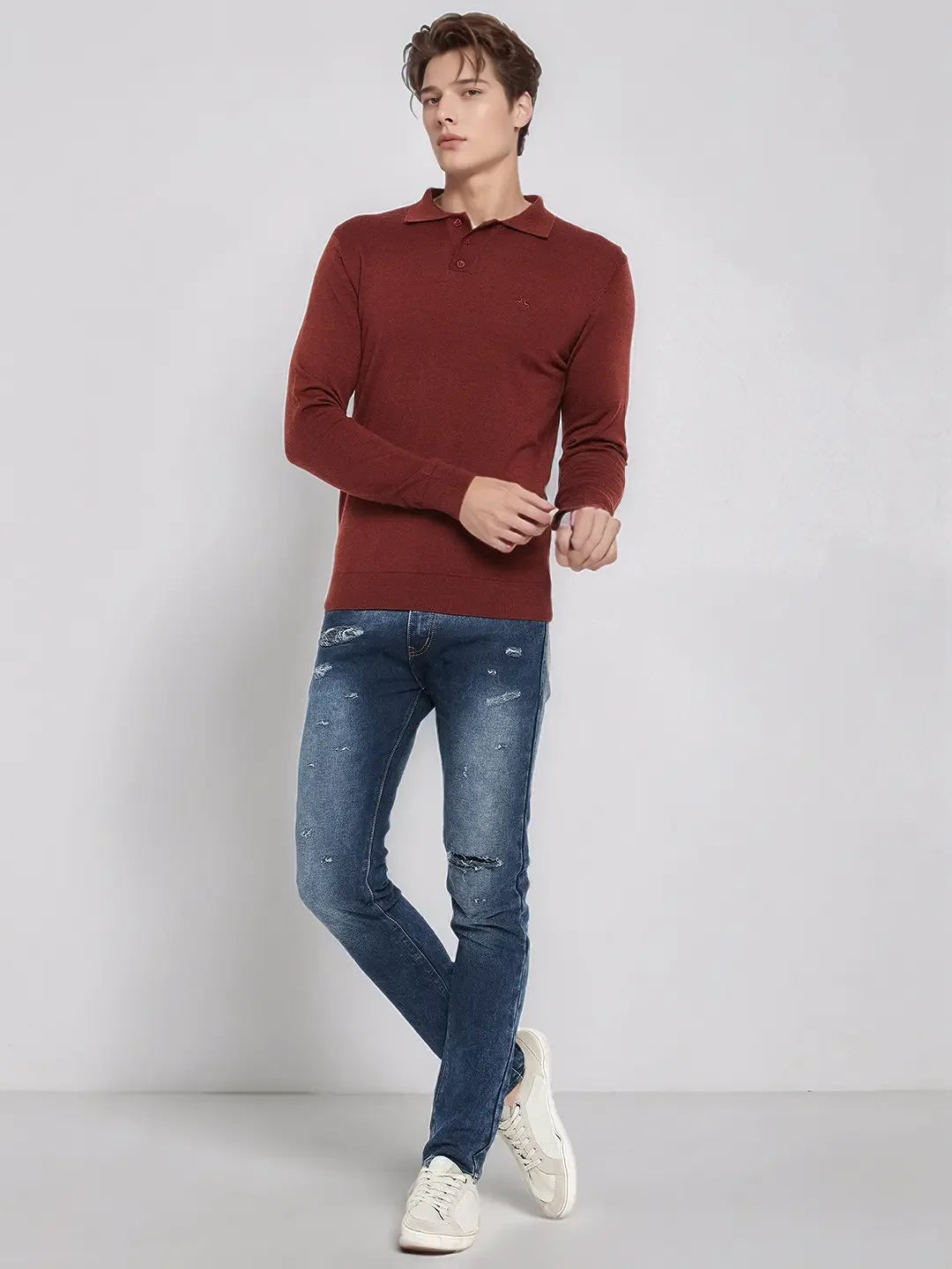 A man wears a 98degreenorth dark maroon merino wool polo neck sweater, blue jeans, and white sneakers.