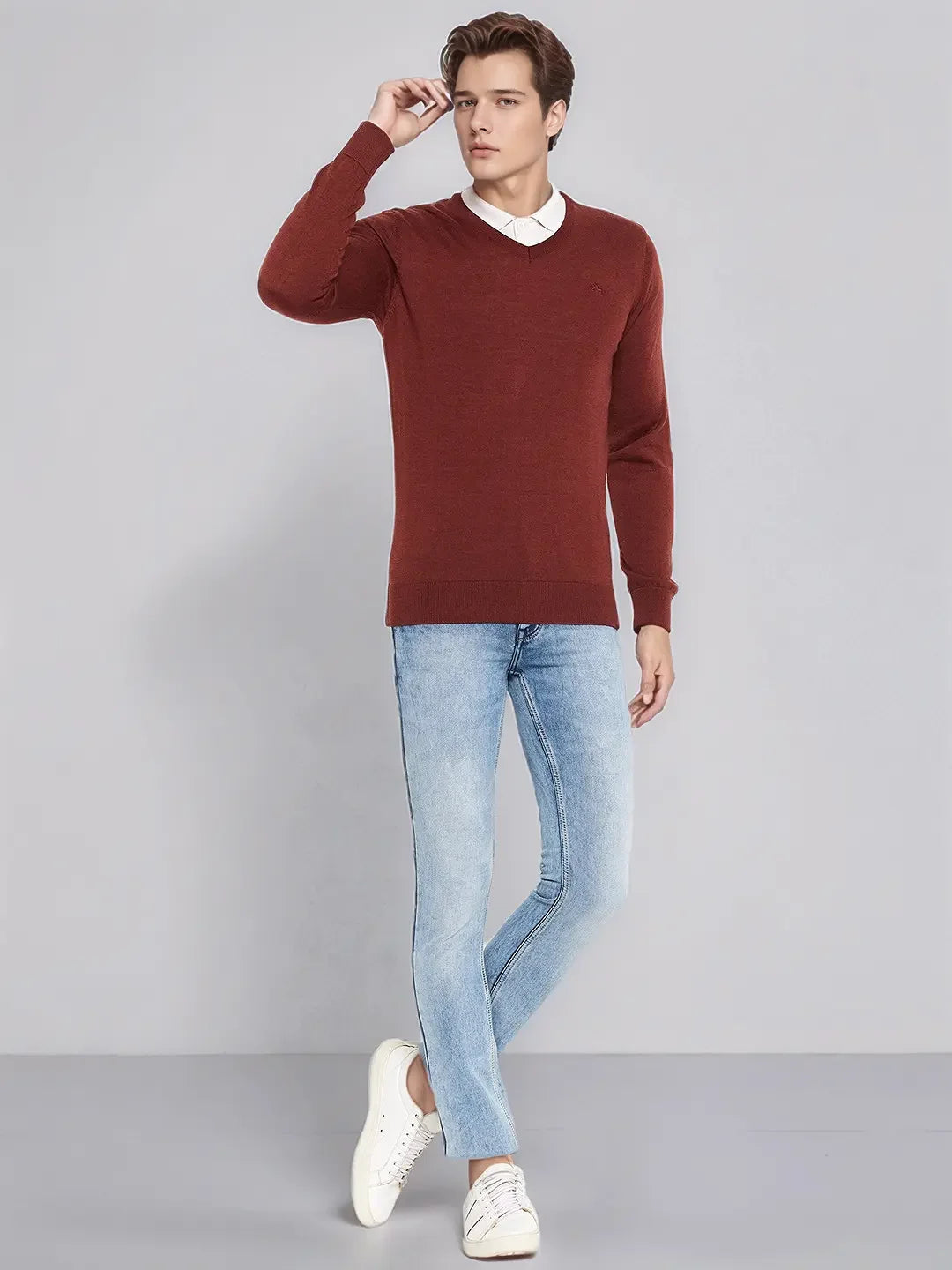 A man in a 98degreenorth Dark Maroon Merino Wool V-Neck Sweater poses in jeans and sneakers against a gray background.