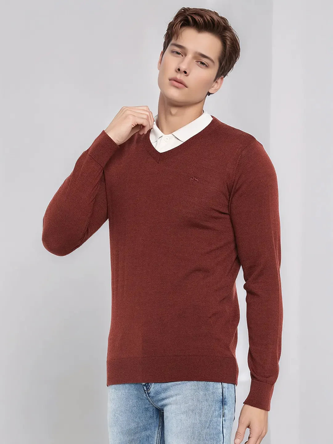 Man wears 98degreenorth Men’s Dark Maroon Merino Wool V-Neck Sweater over a white shirt and jeans against a plain background.