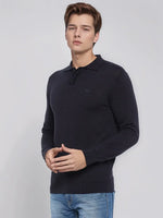 Young man in a 98degreenorth Men’s Dark Navy Merino Wool Polo Sweater and blue jeans stands against a plain light background.