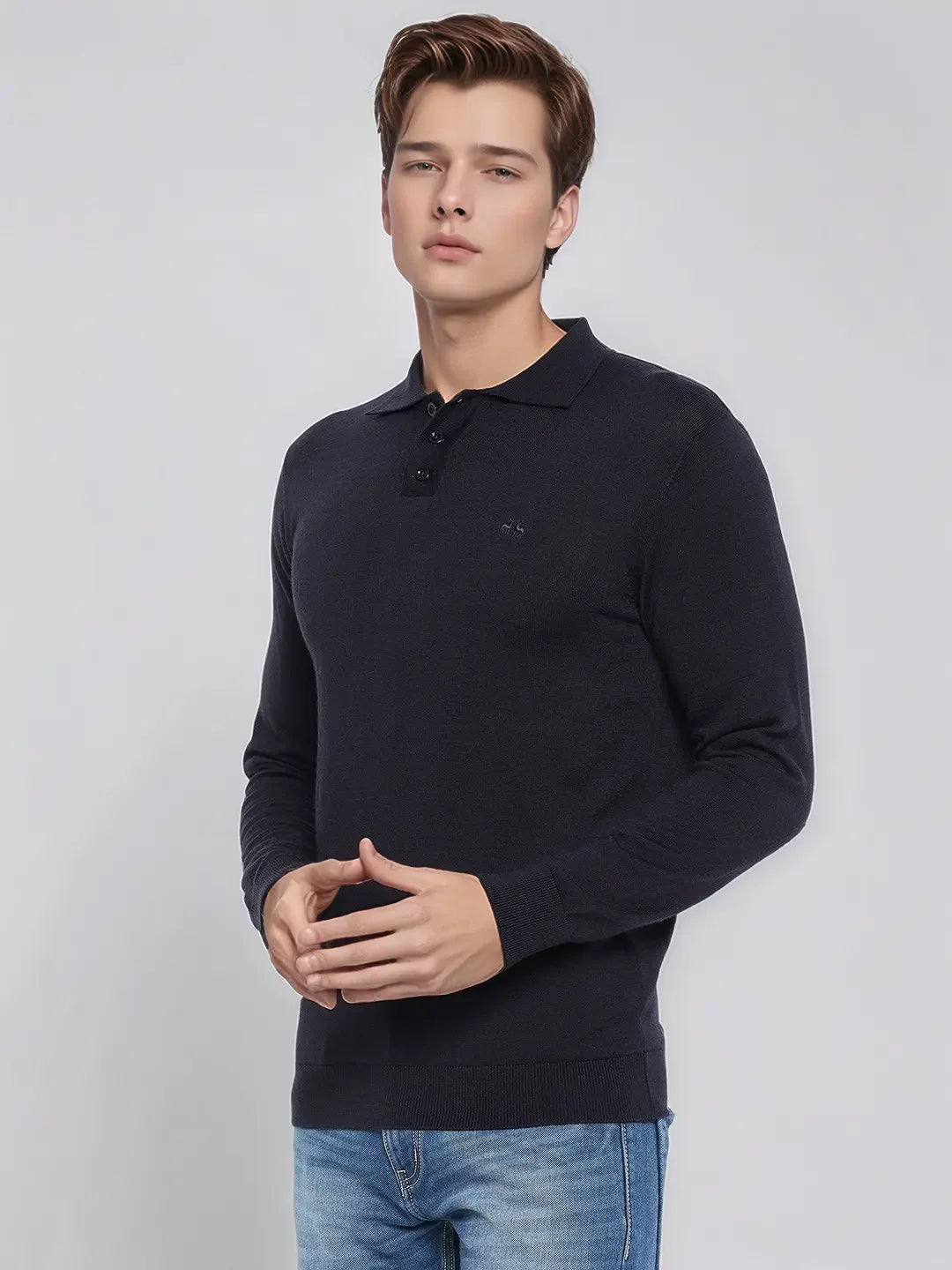 Young man in a 98degreenorth Men’s Dark Navy Merino Wool Polo Sweater and blue jeans stands against a plain light background.