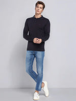 A man in a 98degreenorth dark navy Merino Wool Polo Sweater stands against a plain gray background.