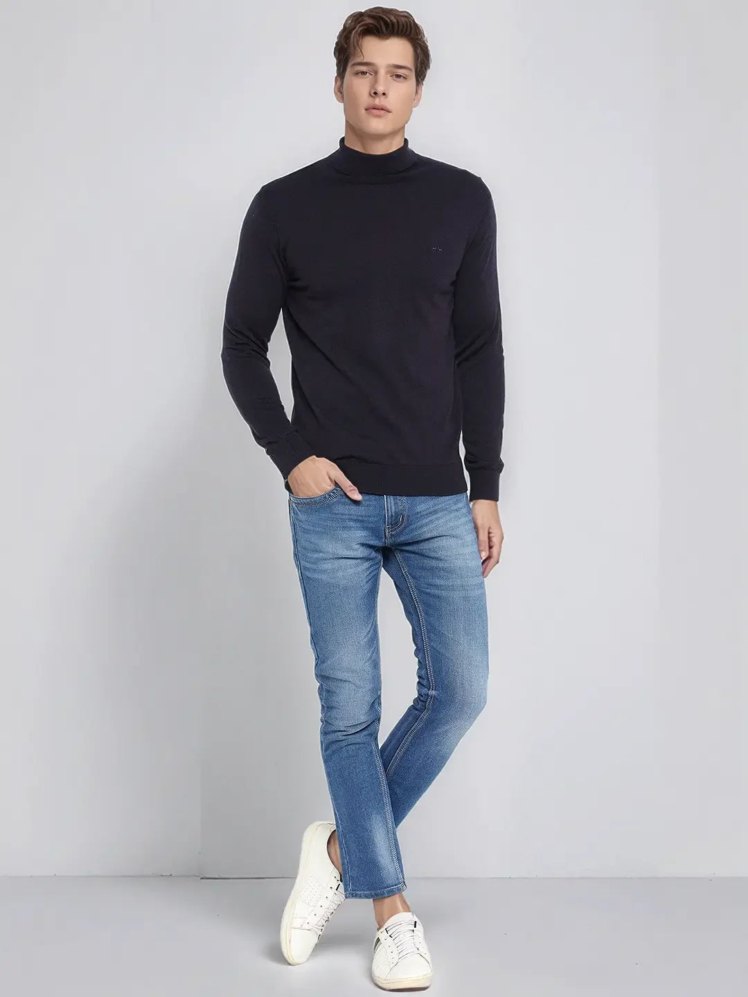 A man wears a 98degreenorth dark navy merino wool turtle neck sweater, blue jeans, and white sneakers.