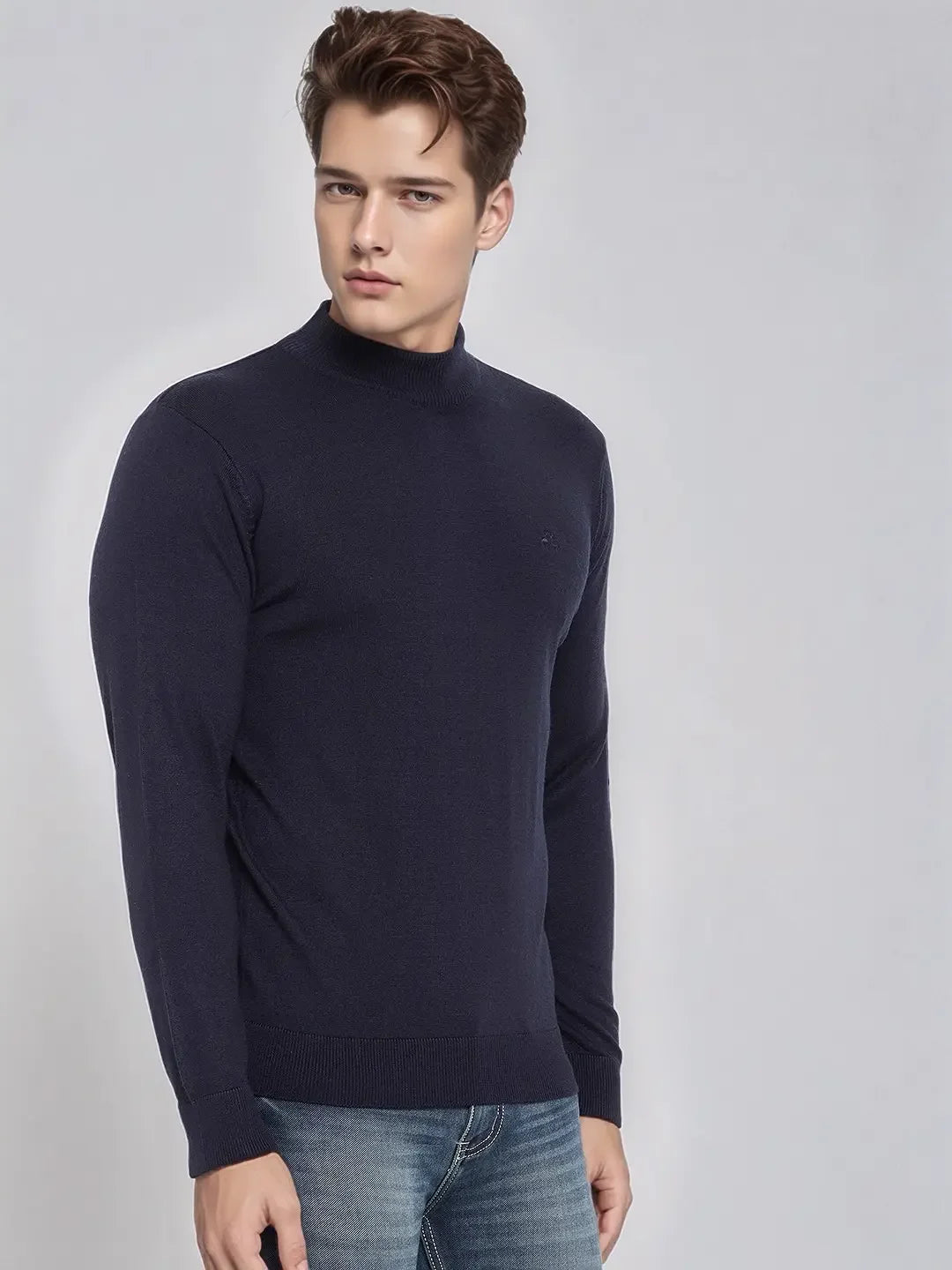 A man wears a 98degreenorth Men’s Dark Navy Merino Wool Turtle Neck Sweater and jeans against a light gray background.