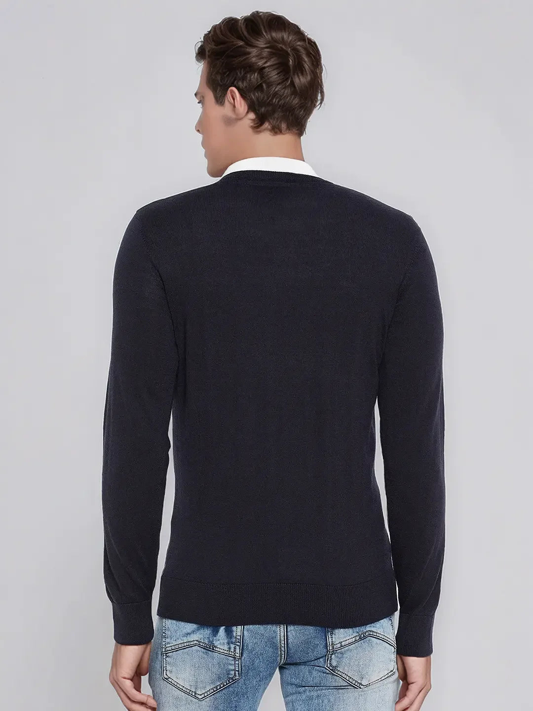 A man wears a 98degreenorth Dark Navy Merino Wool V-Neck Sweater with light blue jeans, facing away from the camera.