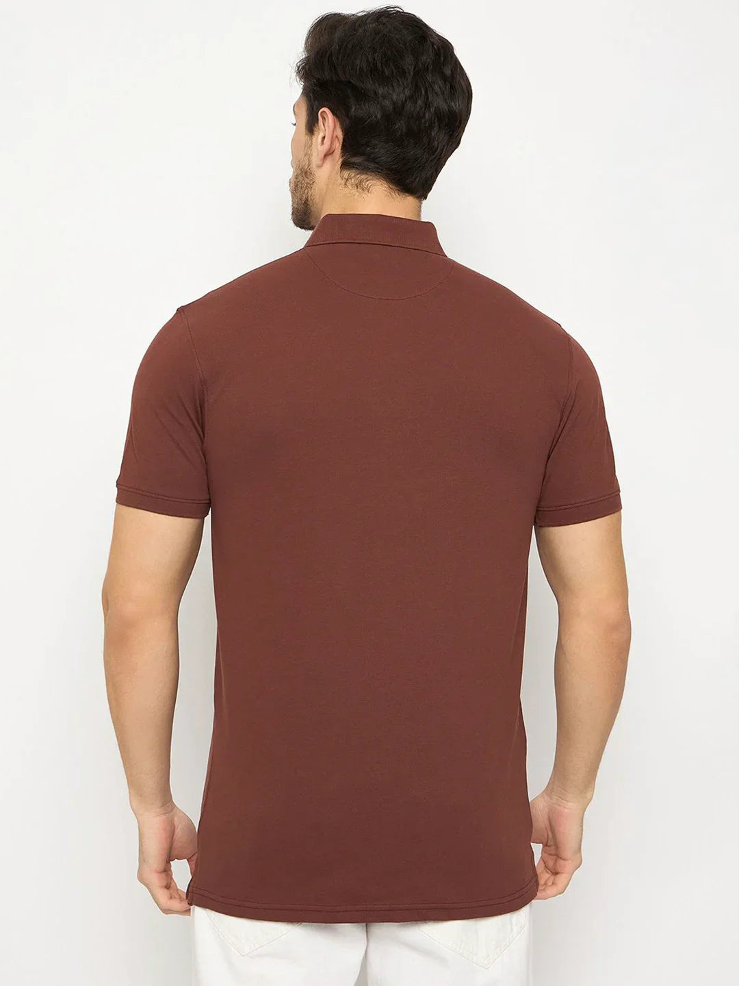 Man facing away in 98degreenorth Men's Dark Rust Polo T-Shirt with chest pocket, stretch cotton pique, and white pants.