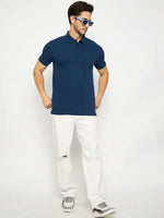 Man in 98degreenorth's denim blue cotton polo with chest pocket, white jeans, gray sneakers, and blue sunglasses.