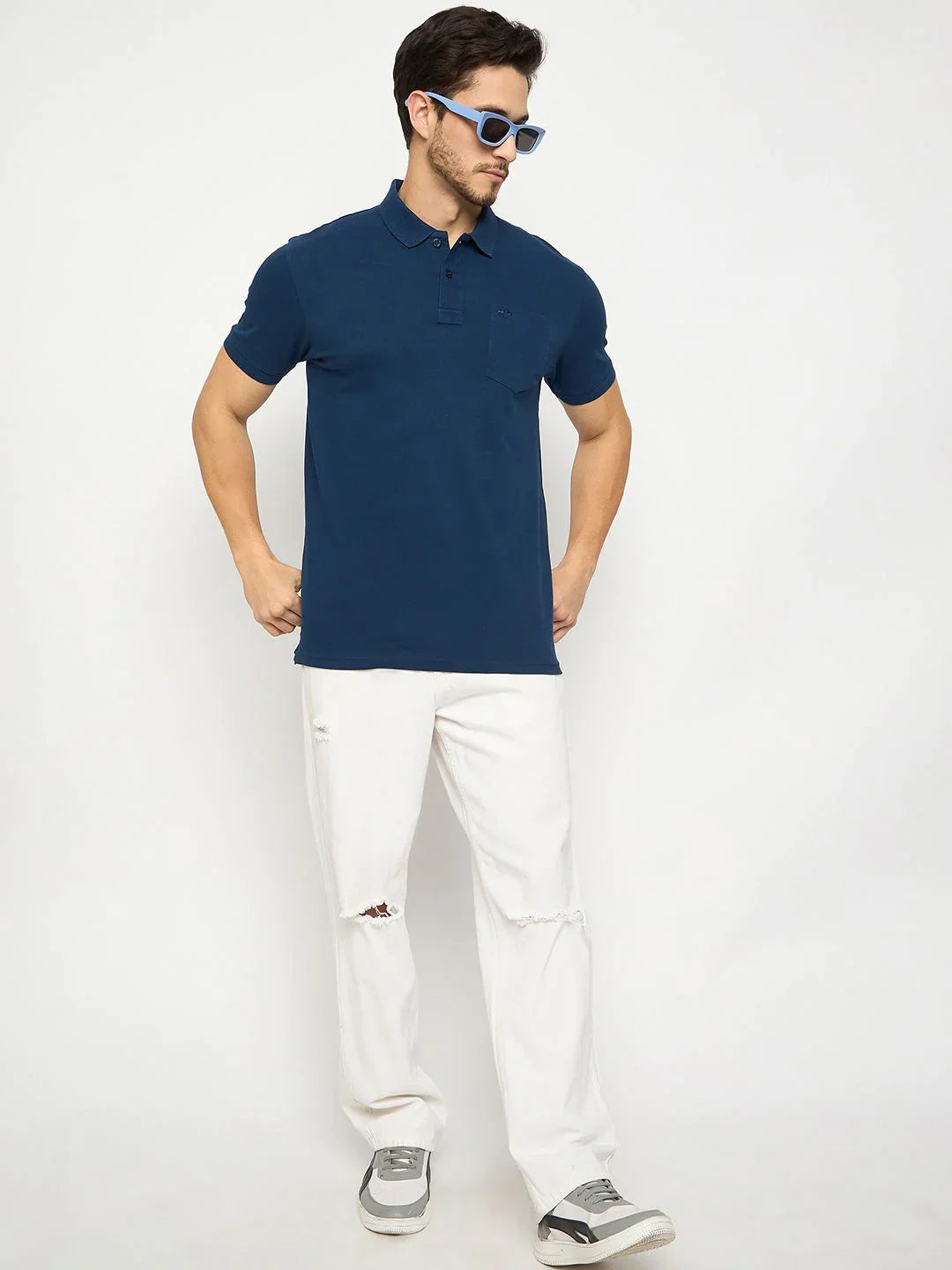 Man in 98degreenorth's denim blue cotton polo with chest pocket, white jeans, gray sneakers, and blue sunglasses.