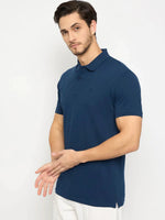 Man in 98degreenorth Men's Denim Blue Solid Cotton Pique Polo, paired with white pants against a white background.