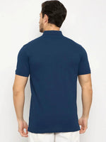 Man wearing 98degreenorth Men's Denim Blue Solid Polo T-Shirt—Cotton Pique, facing away in white pants.