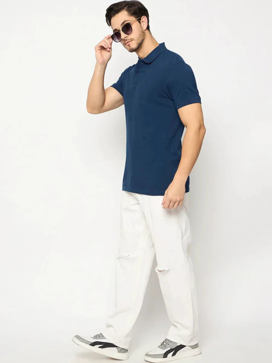 Man wearing 98degreenorth Men's Denim Blue Solid Polo T-Shirt stands against a plain white background.