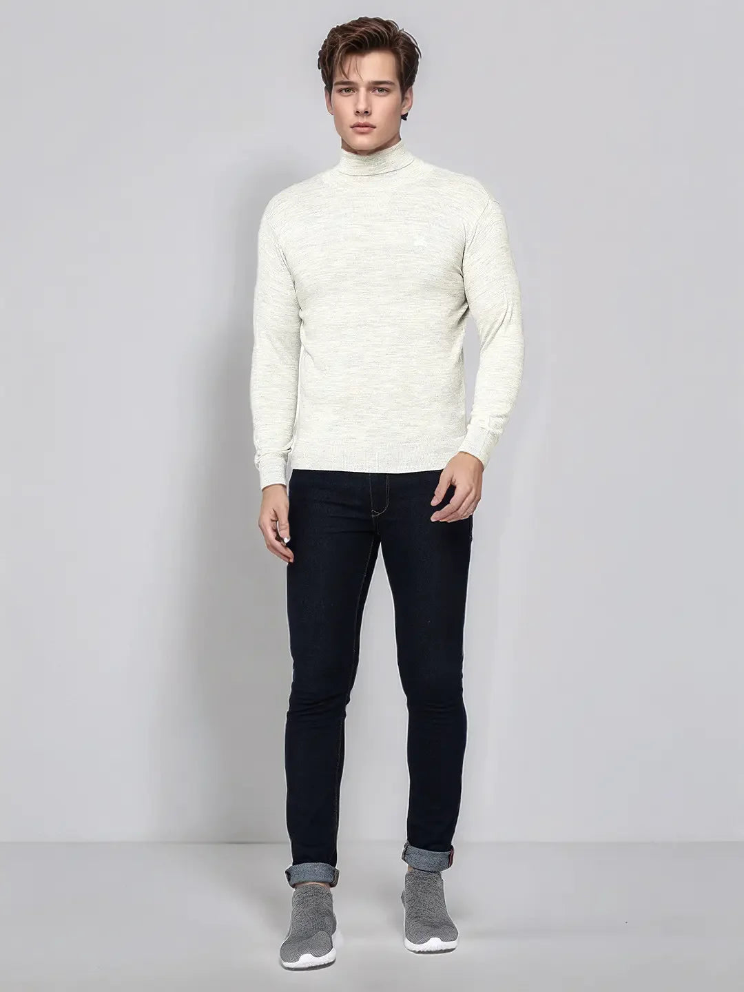 A man wears a 98degreenorth Men's Ecru Merino Wool Turtle Neck Sweater, dark jeans, and gray slip-on shoes.
