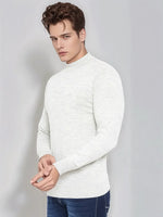 Man wears 98degreenorth Men’s Ecru Merino Wool Turtle Neck Sweater and blue jeans, posing against a gray background.