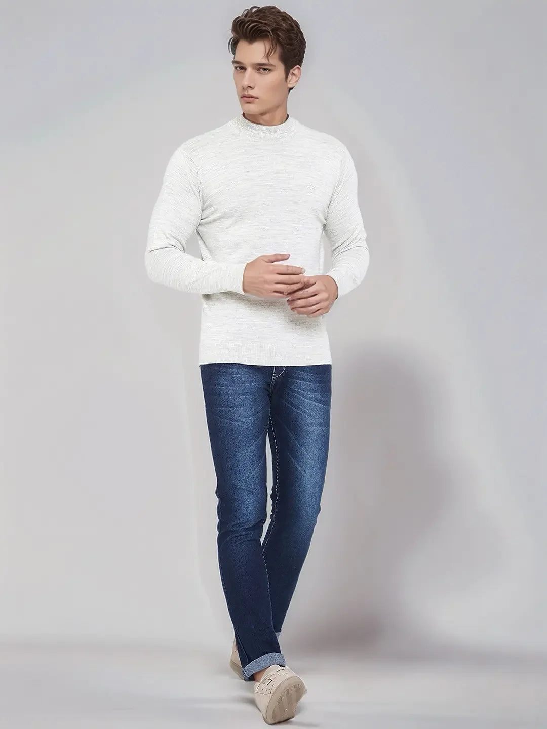 A man in 98degreenorth’s ecru merino wool turtle neck sweater pairs it with blue jeans and beige shoes.