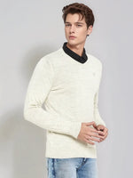 A young man wears a 98degreenorth Men’s Ecru Merino Wool V-Neck Sweater and blue jeans against a light gray background.