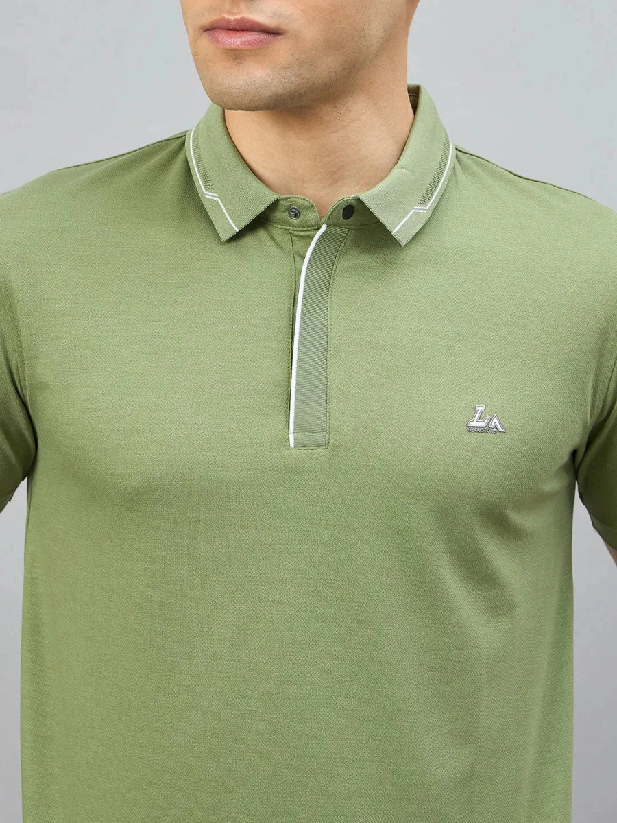 A person wears the 98degreenorth Men's Green Polo T-Shirt with White Tipping and LA Logo—classic men's style.