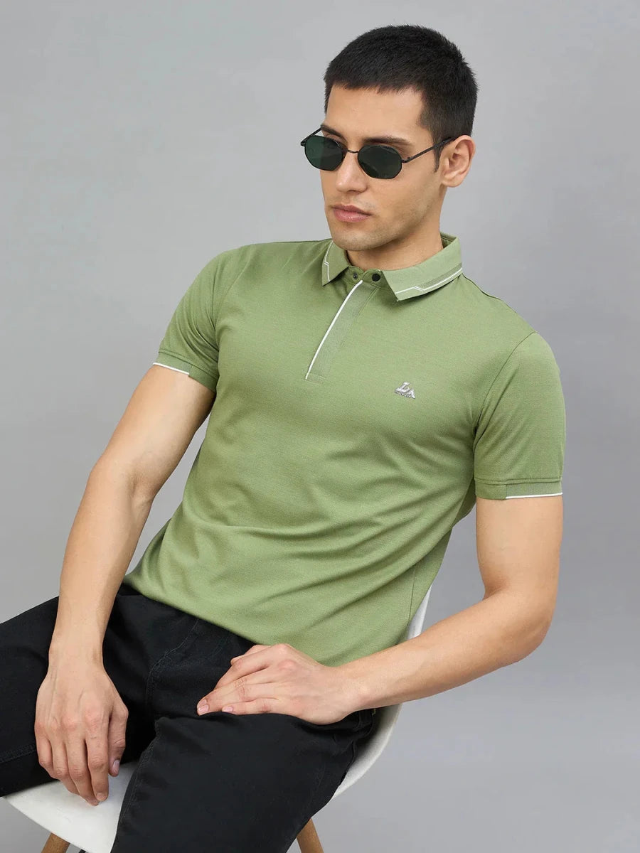 Man in 98degreenorth’s green LA Logo polo with white tipping, sitting on a chair against a gray background.