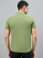 A man in a 98degreenorth Men's Green Polo T-Shirt with White Tipping stands stylishly against a gray backdrop.