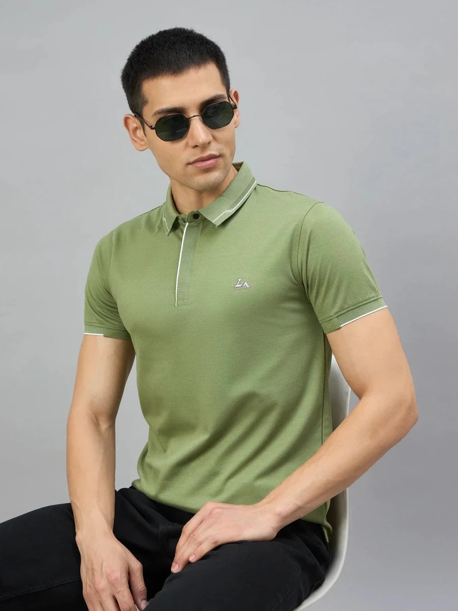 Man in 98degreenorth's Men's Green Polo with White Tipping & LA Logo, seated on a chair against a gray background.