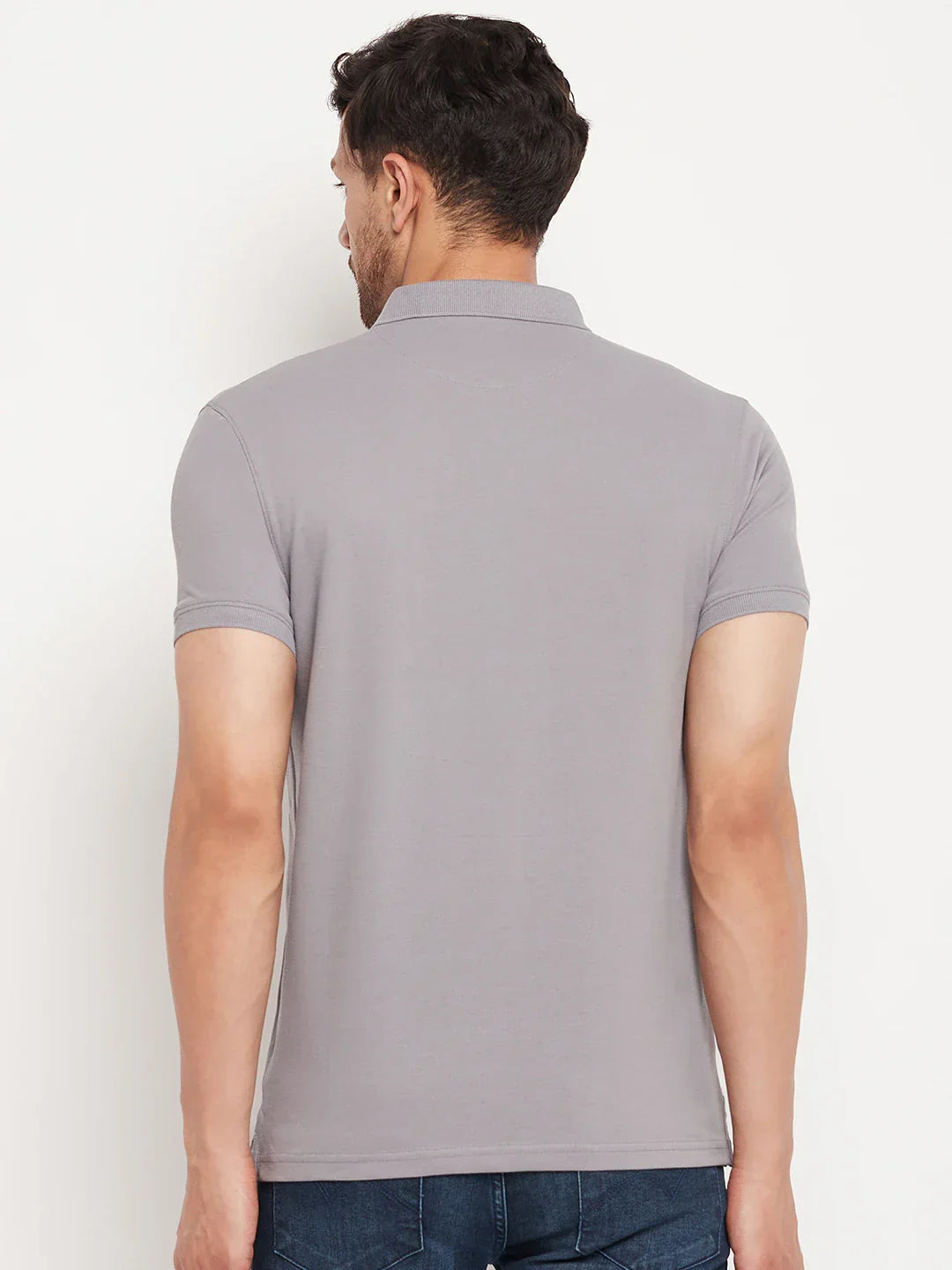 Man wears 98degreenorth Men's Grey Stretch Cotton Pique Polo with chest pocket, back to camera, on white background.