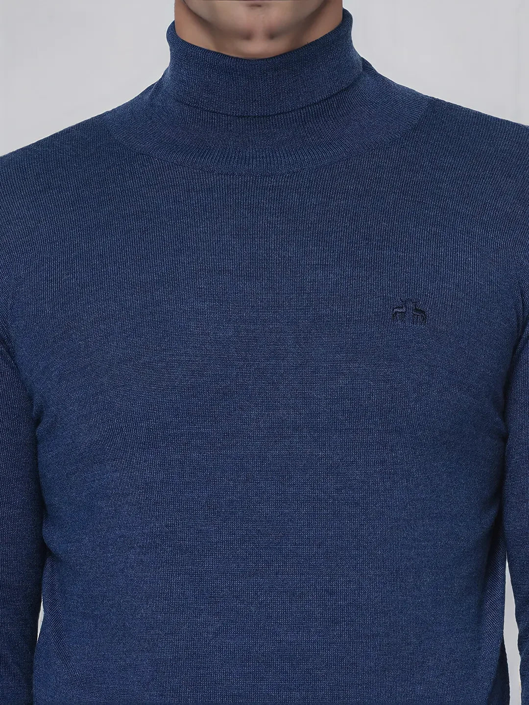 A person wears the 98degreenorth Men’s Light Denim Merino Wool Turtle Neck Sweater with an embroidered chest logo.