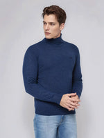 A man wears the 98degreenorth Men’s Light Denim Merino Wool Turtle Neck Sweater against a plain light gray background.
