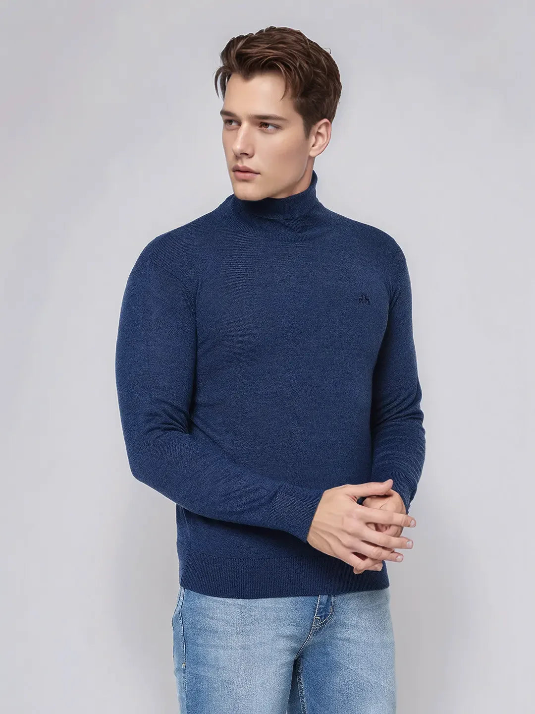 A man wears the 98degreenorth Men’s Light Denim Merino Wool Turtle Neck Sweater against a plain light gray background.