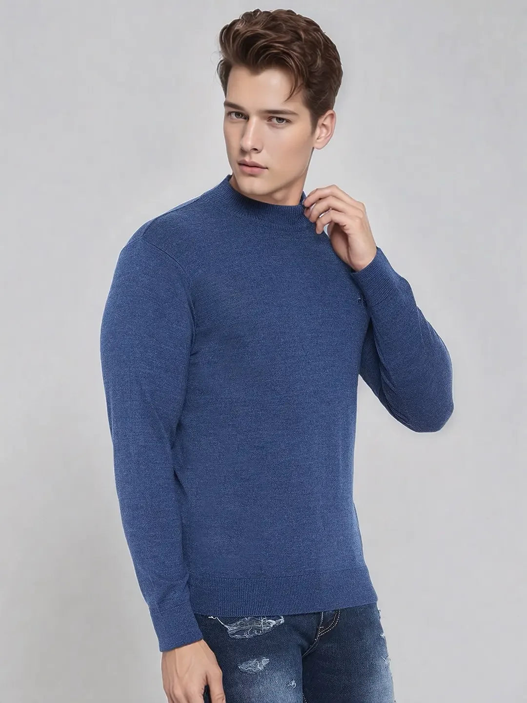 A young man wears the 98degreenorth Men’s Light Denim Merino Wool Turtle Neck Sweater against a light gray background.