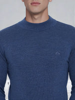 A man wearing a 98degreenorth Men’s Light Denim Merino Wool Turtle Neck Sweater with a small white chest logo.