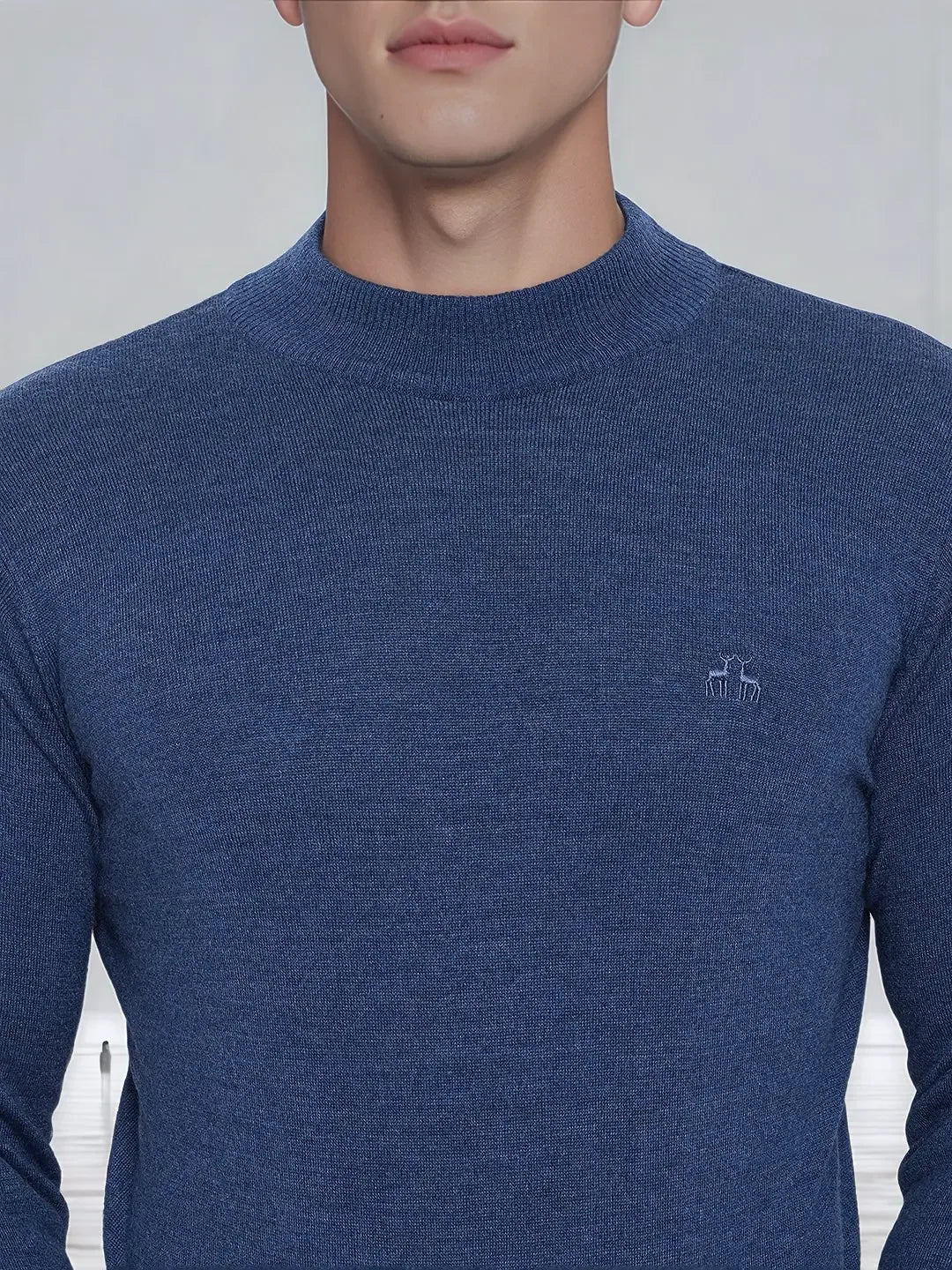 A man wearing a 98degreenorth Men’s Light Denim Merino Wool Turtle Neck Sweater with a small white chest logo.