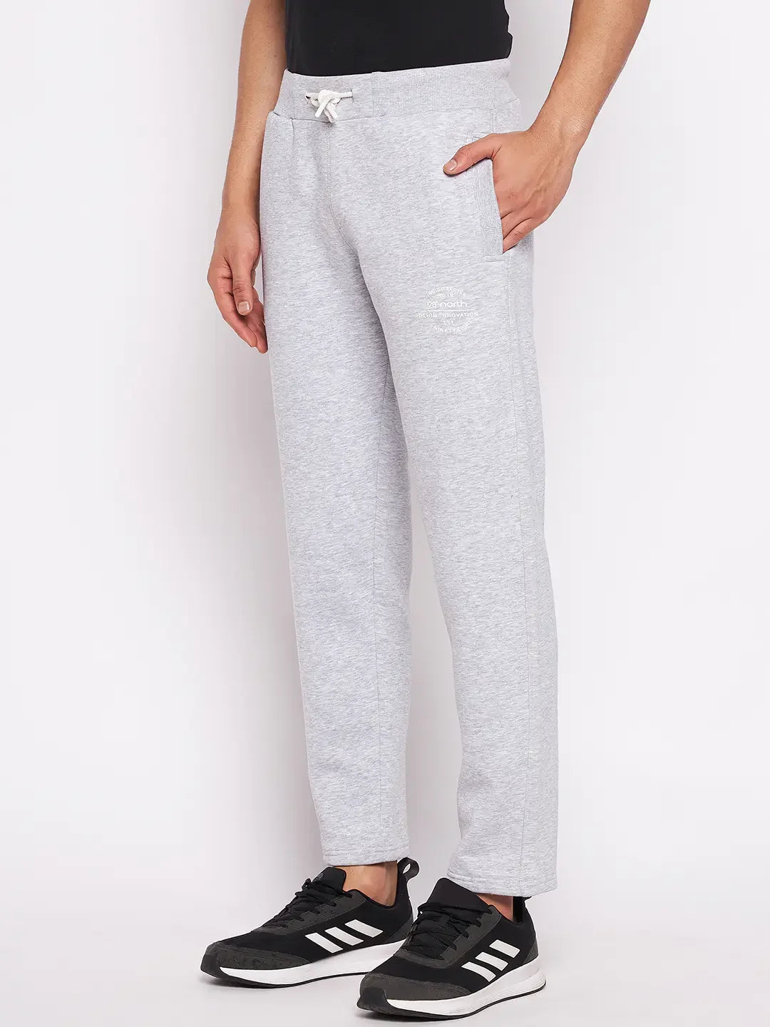 Man wears 98degreenorth Men’s Light Grey Fleece Trackpants with adjustable drawstring and black Adidas sneakers, hand in pocket.