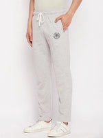 A man wears 98degreenorth Men's Light Grey French Terry Lycra Trackpants, styled with white sneakers against a plain backdrop.
