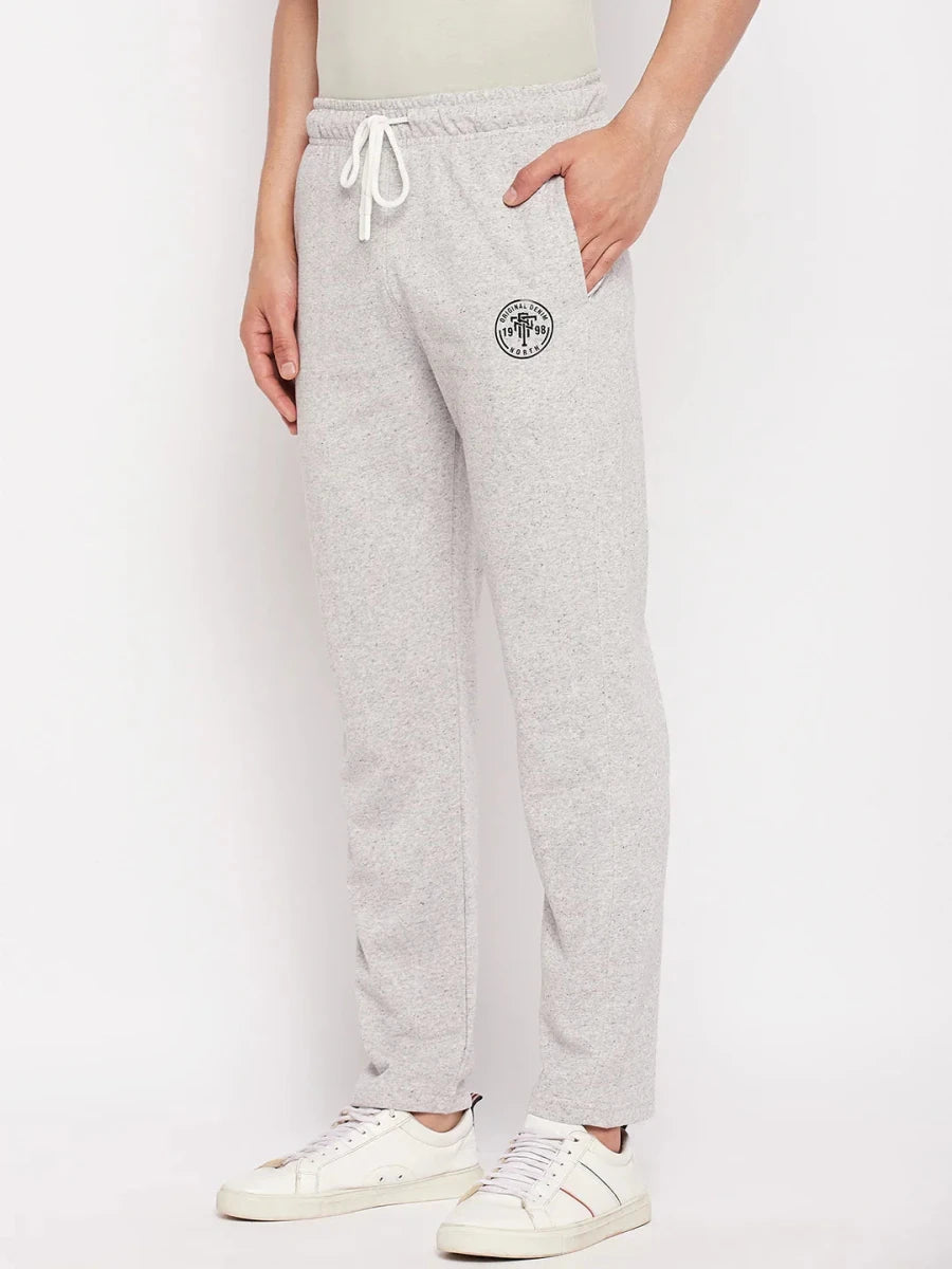 A man wears 98degreenorth Men's Light Grey French Terry Lycra Trackpants, styled with white sneakers against a plain backdrop.