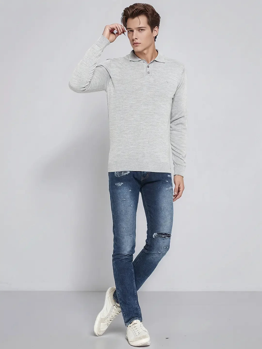 Man in 98degreenorth’s Light Grey Merino Wool Polo Sweater, blue jeans & white sneakers, against a plain background.