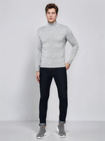 A man in a 98degreenorth Men’s Light Grey Merino Wool Turtle Neck Sweater and dark jeans stands against a plain background.