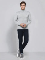 A man in a 98degreenorth light grey merino wool turtle neck sweater and dark jeans stands against a plain background.
