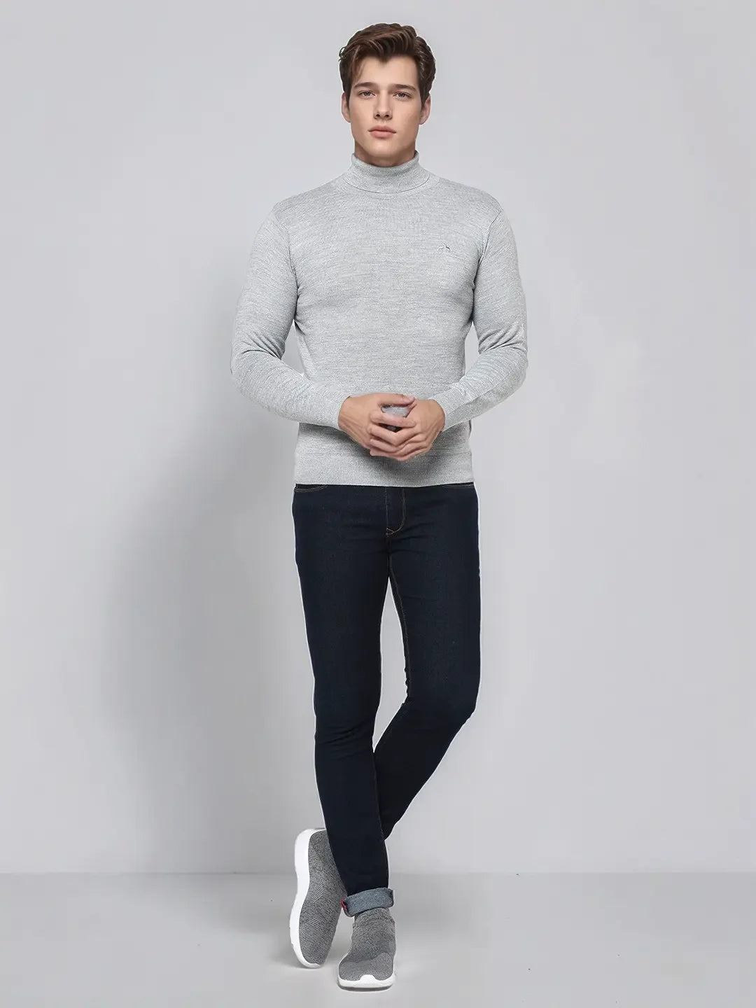 A man in a 98degreenorth light grey merino wool turtle neck sweater and dark jeans stands against a plain background.