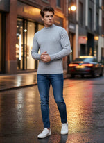 A man wears the 98degreenorth Men’s Light Grey Merino Wool Turtleneck Sweater on a wet city street at dusk.