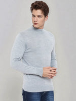 A man in 98degreenorth light grey merino wool turtle neck sweater poses in blue jeans against a plain grey background.