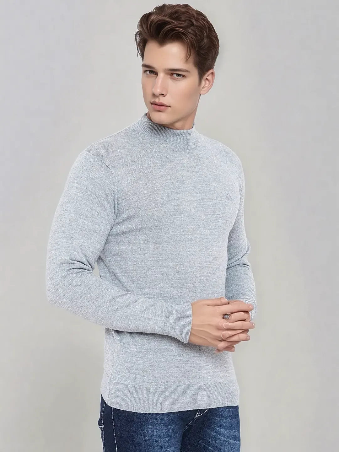A man in 98degreenorth light grey merino wool turtle neck sweater poses in blue jeans against a plain grey background.