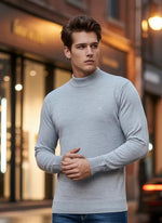 A man wears a 98degreenorth Men’s Light Grey Merino Wool Turtle Neck Sweater while standing outside in the city.