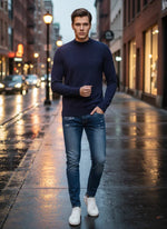 A man in a 98degreenorth Light Navy Merino Wool Turtle Neck Sweater walks on a wet city street at dusk.
