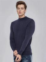 A man wears a 98degreenorth Men’s Light Navy Merino Wool Turtle Neck Sweater, standing against a light gray background.