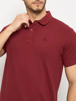 Man wears 98degreenorth Men's Maroon Solid Polo T-Shirt in cotton pique, touching the collar against a plain background.