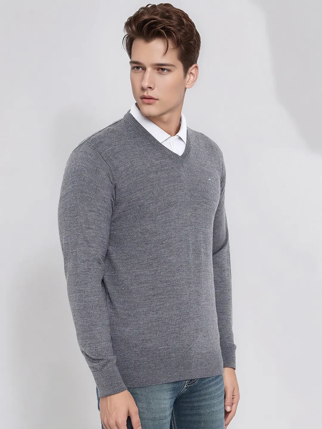 A man wears a 98degreenorth Men’s Medium Grey Merino Wool V-Neck Sweater over a white shirt and blue jeans.
